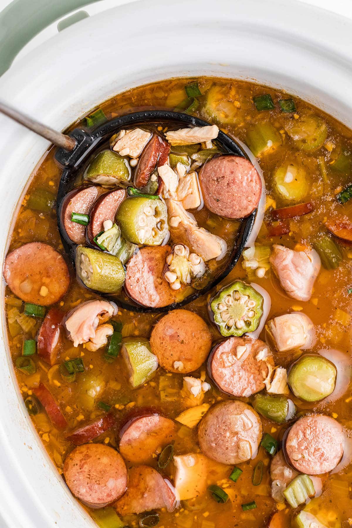 Slow cooker filled with chicken and sausage gumbo with a serving ladle.