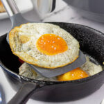 Fried eggs in a cast iron skillet with a spatula.