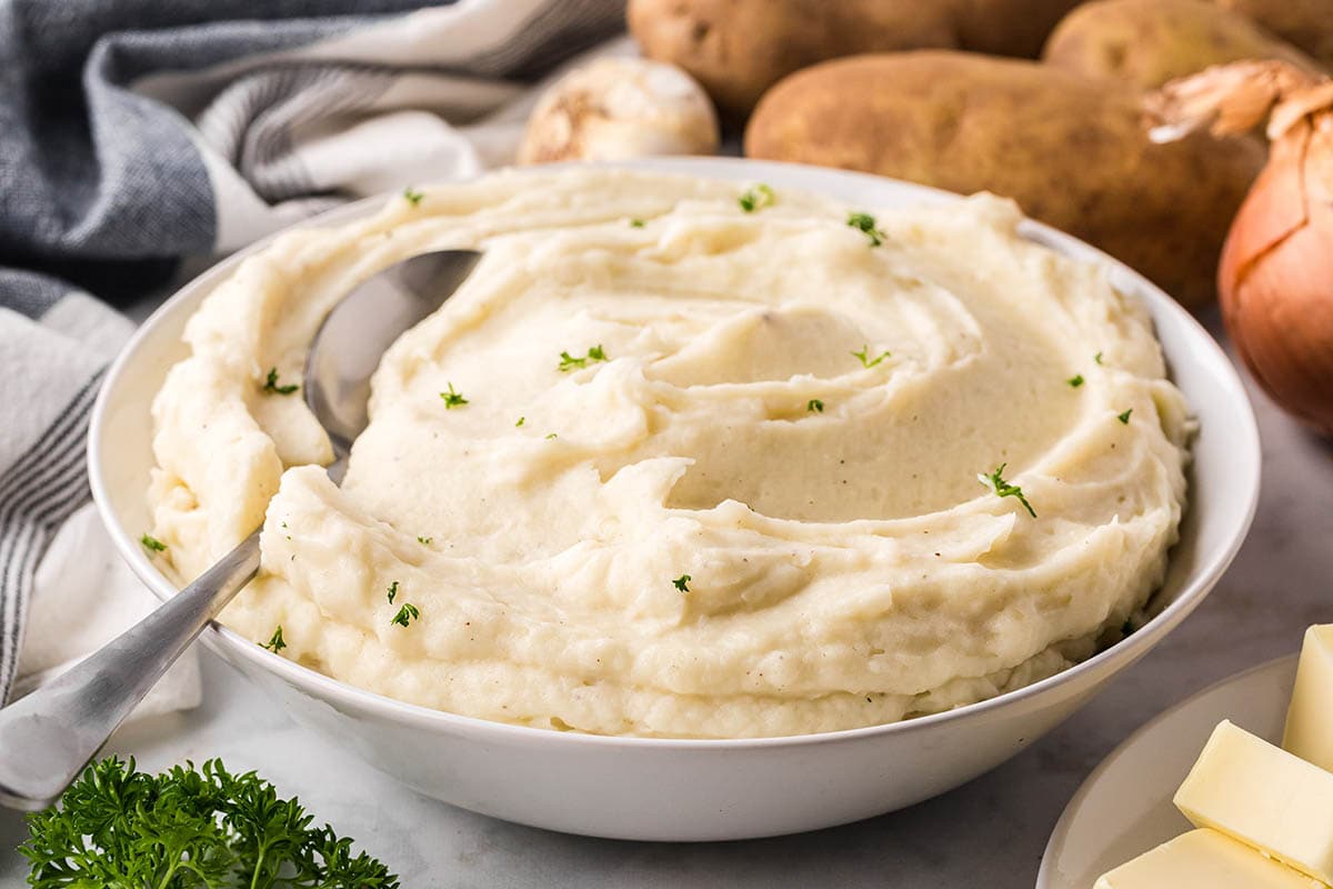 A bowl filled with mashed potatoes, with a serving spoon.