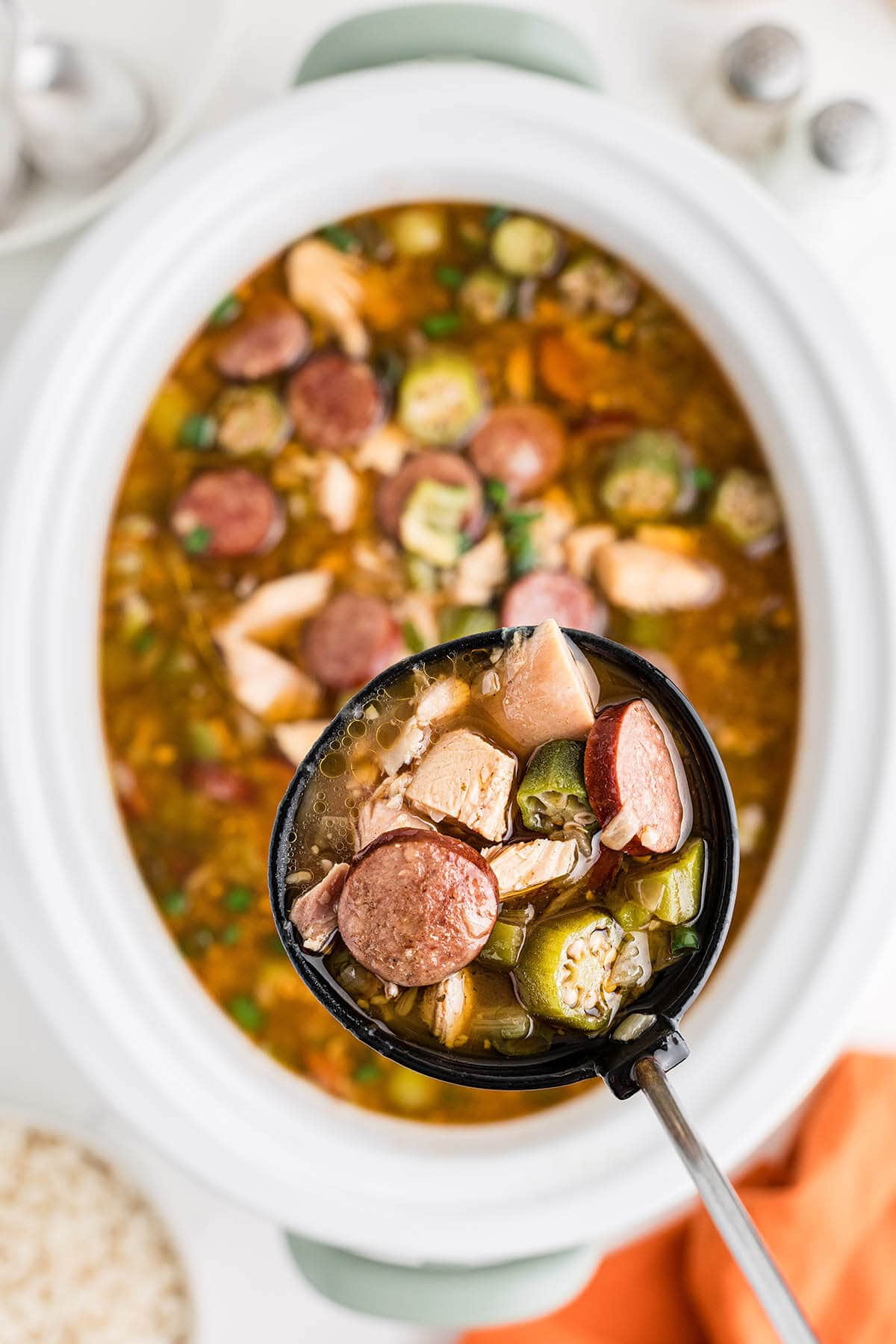 Crockpot filled with Chicken and Sausage Gumbo with ladle scooping up a serving.