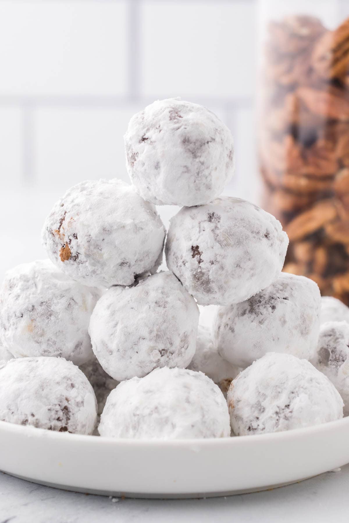 A stack of powered sugar covered pecan bourbon balls on a plate.