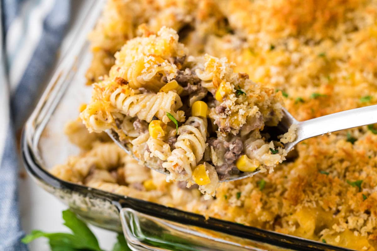 Cheesy hamburger and corn casserole in baking dish with a serving spoon.