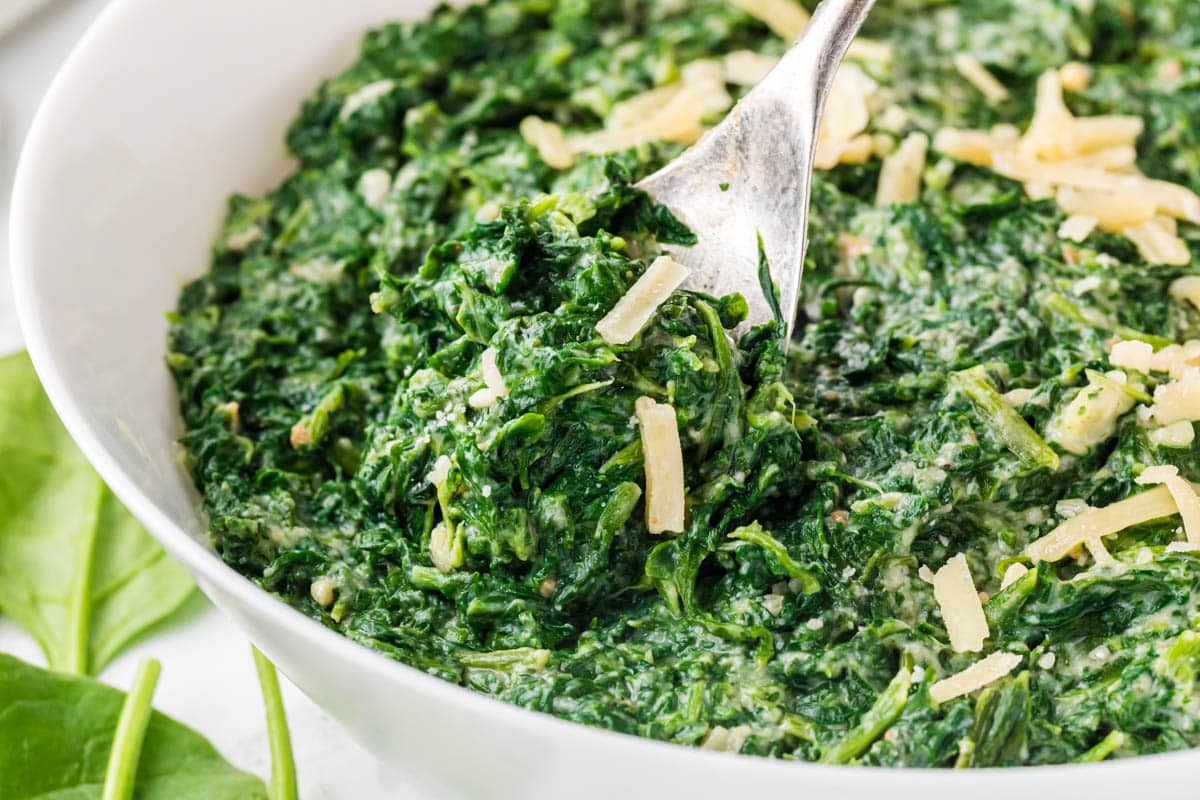 Bowl filled with creamed spinach with a serving spoon.
