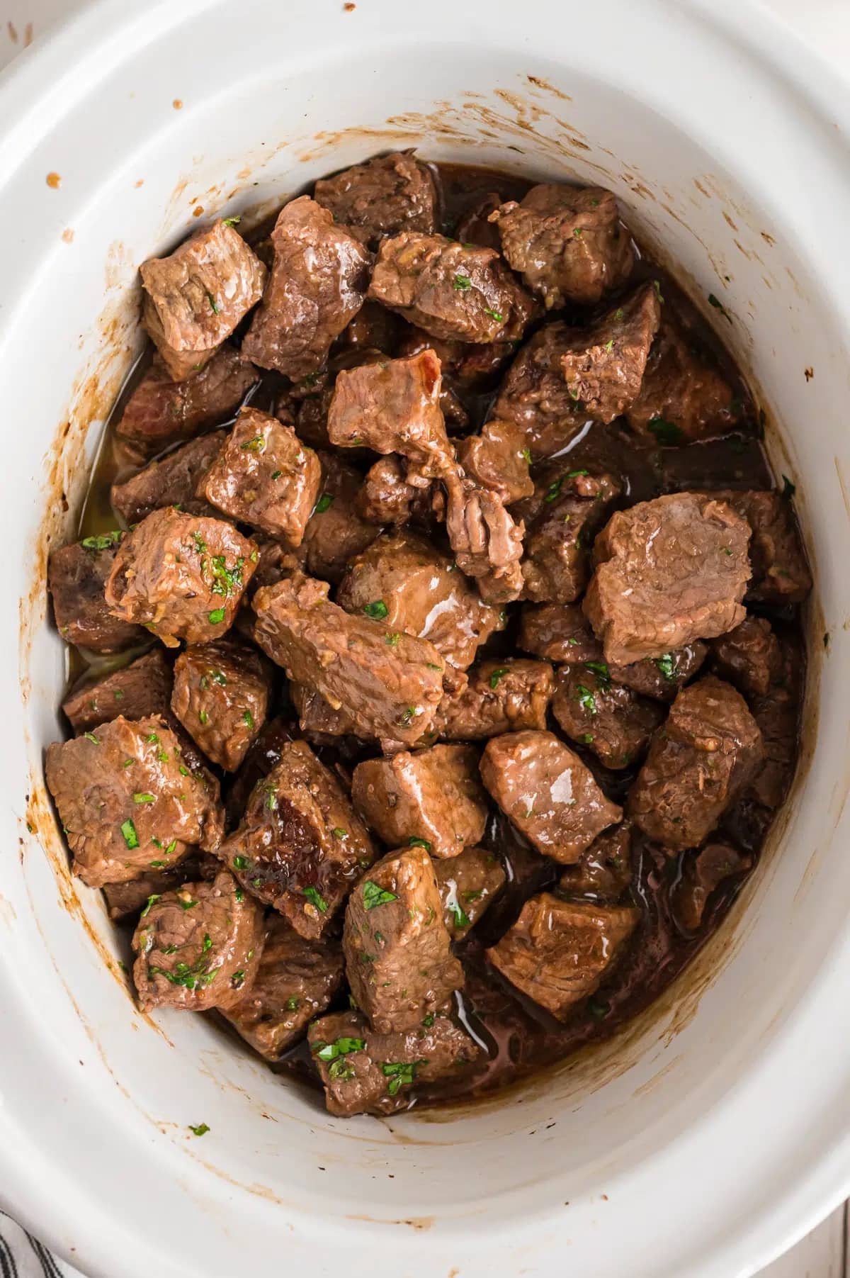 Steak bites in a slow cooker garnished with parsley.