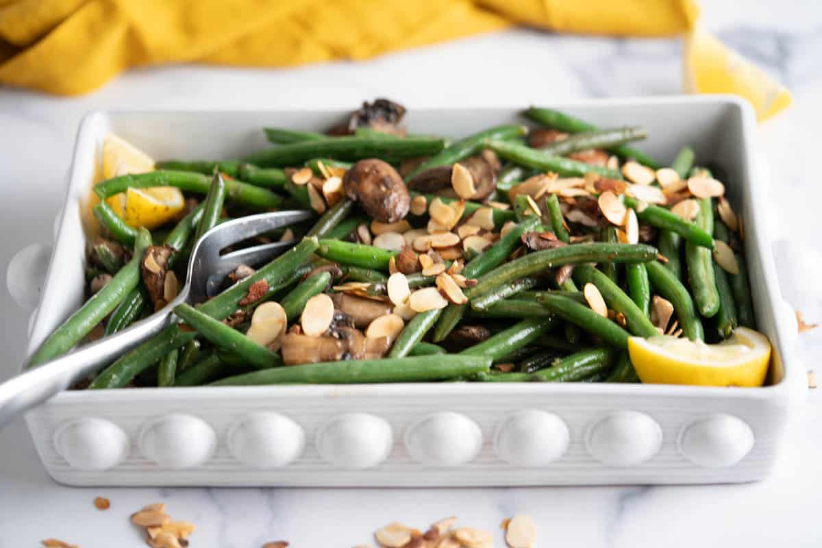 Baking dish filled with fresh green bean casserole topped with toasted almonds and sauteed mushrooms.