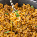 Homemade Hamburger Helper in a skillet with a serving spoon dishing up a scoop.