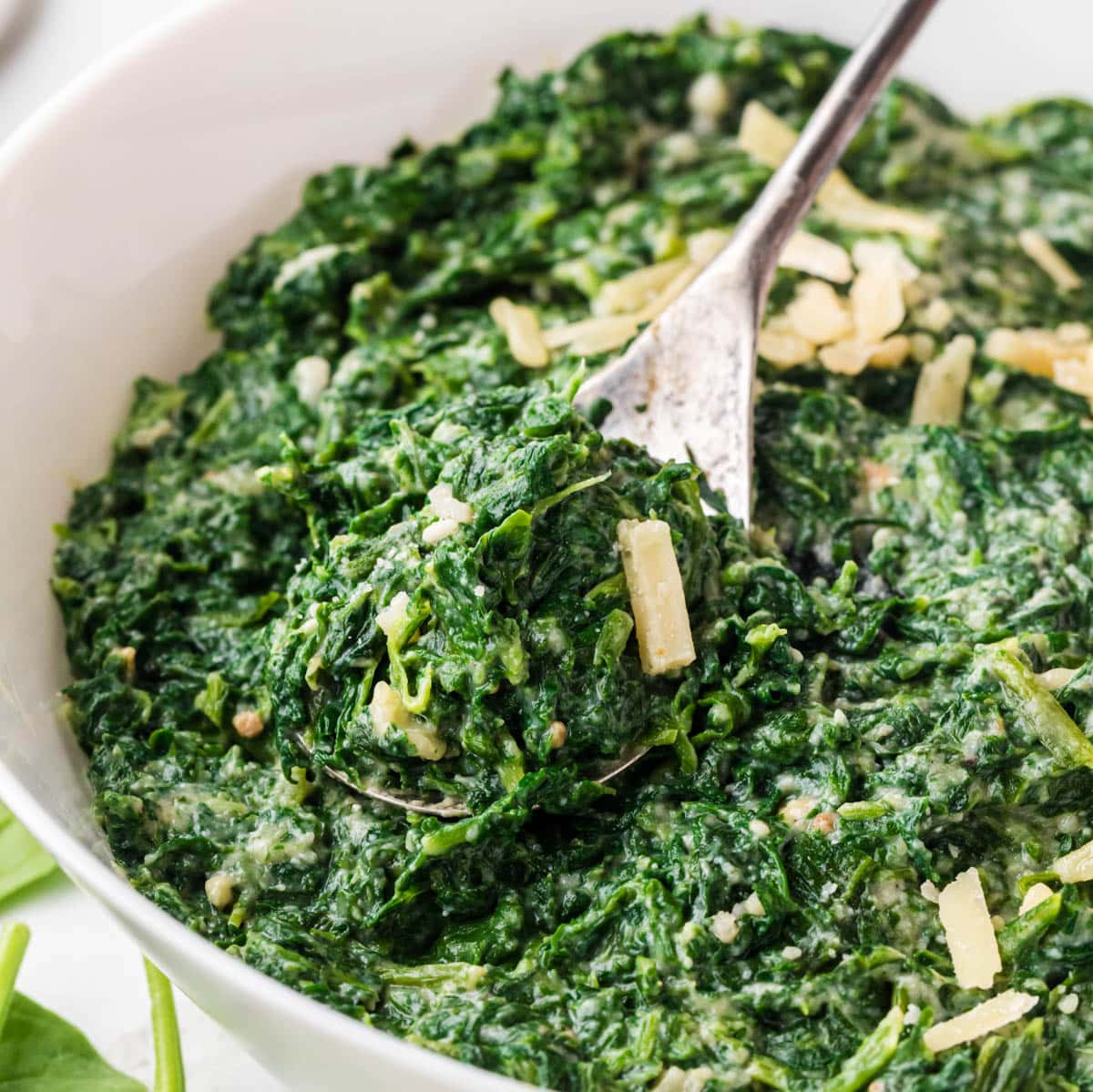 A large white bowl filled with Ruth Chris Steamed Spinach Recipe, with a serving spoon.