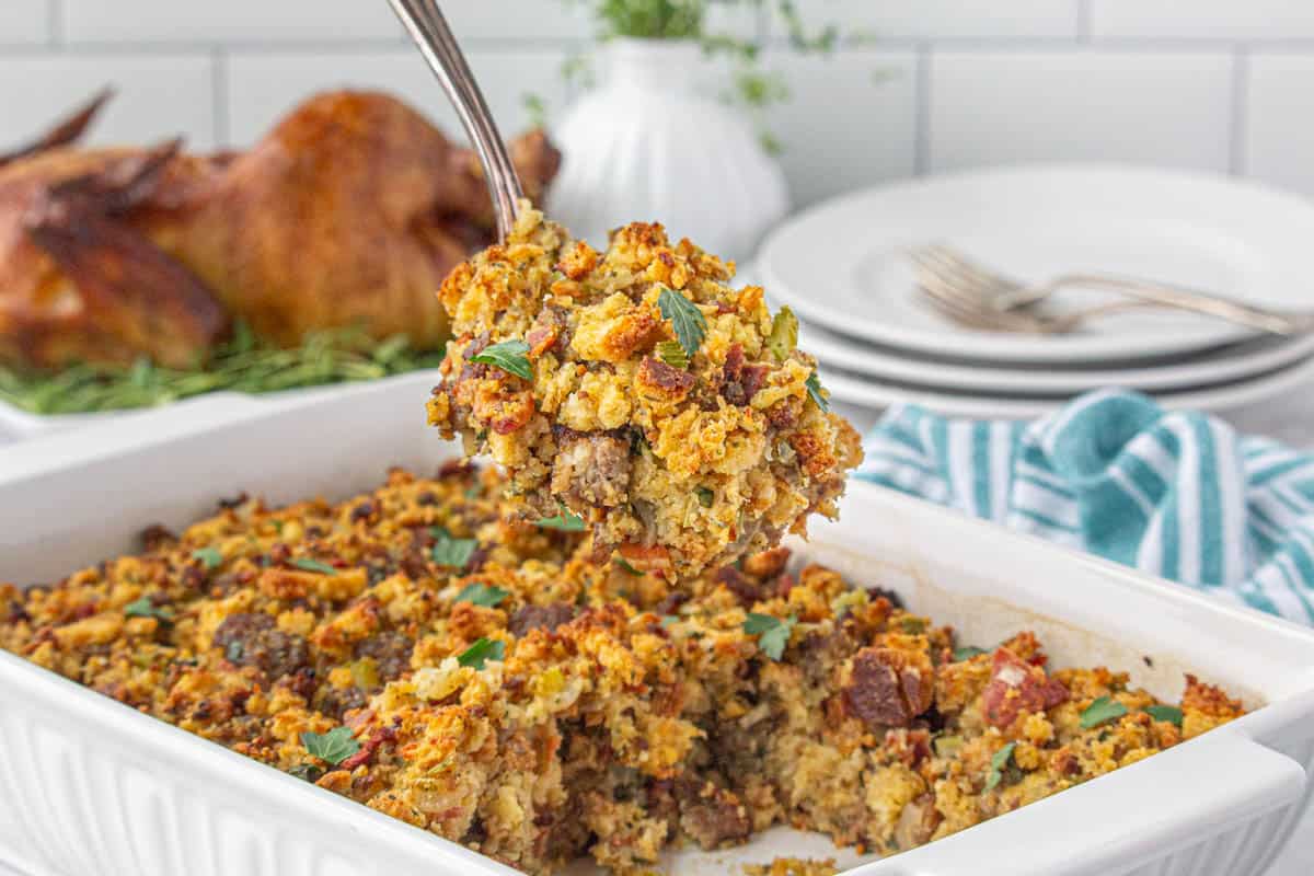 A casserole dish filled with stuffing with a serving spoon taking out a big scoop.
