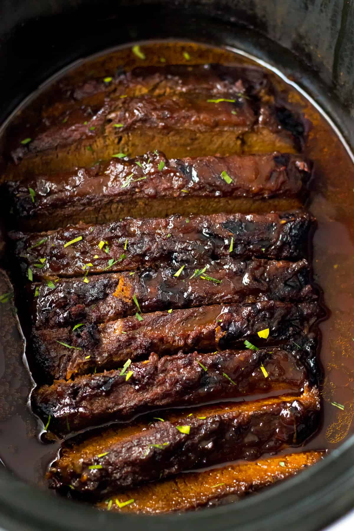 Sliced brisket in barbecue sauce in a baking dish topped.