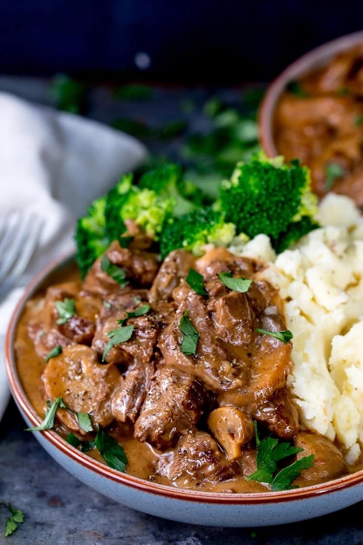 Steak Diane in a bowl, served with mashed potatoes and broccoli.