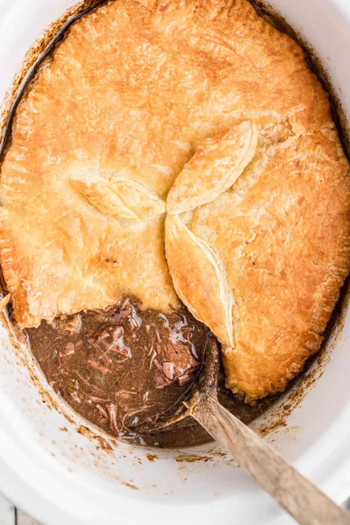 Steak Pie with a beautifully brown crust. There's a spoon dishing up a serving.