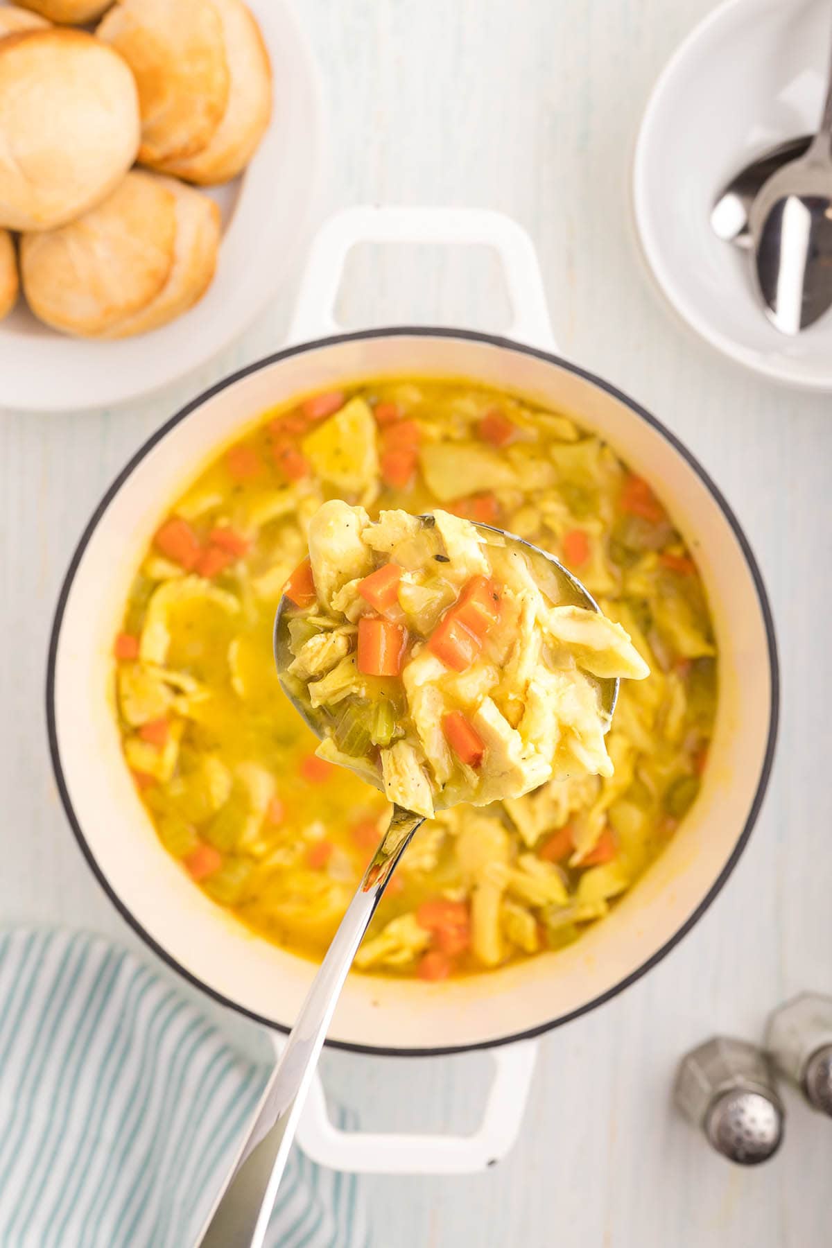 A pot of homemade Chicken and Dumpling Soup in a soup pot, with a ladle scooping out a serving.