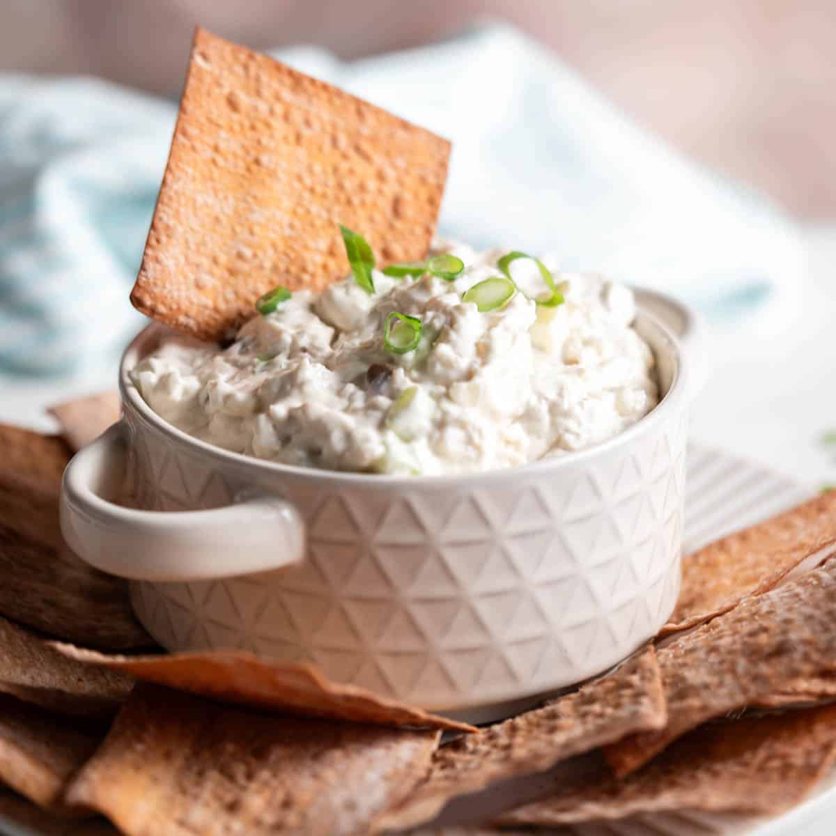 A bowl filled with crab dip with a wonton chip placed into the dip.