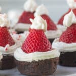 Brownies topped with frosting and a fresh strawberry, decorated to look like Santa hats.