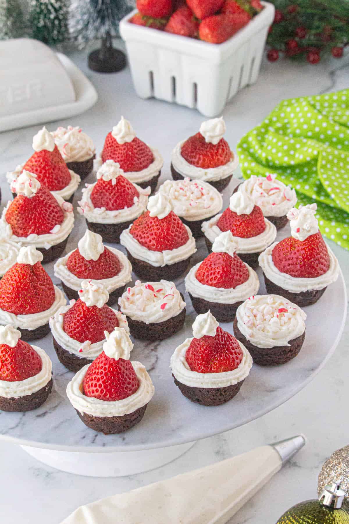A platter filled with brownies topped with fresh strawberries and decorated look like Santa hats.
