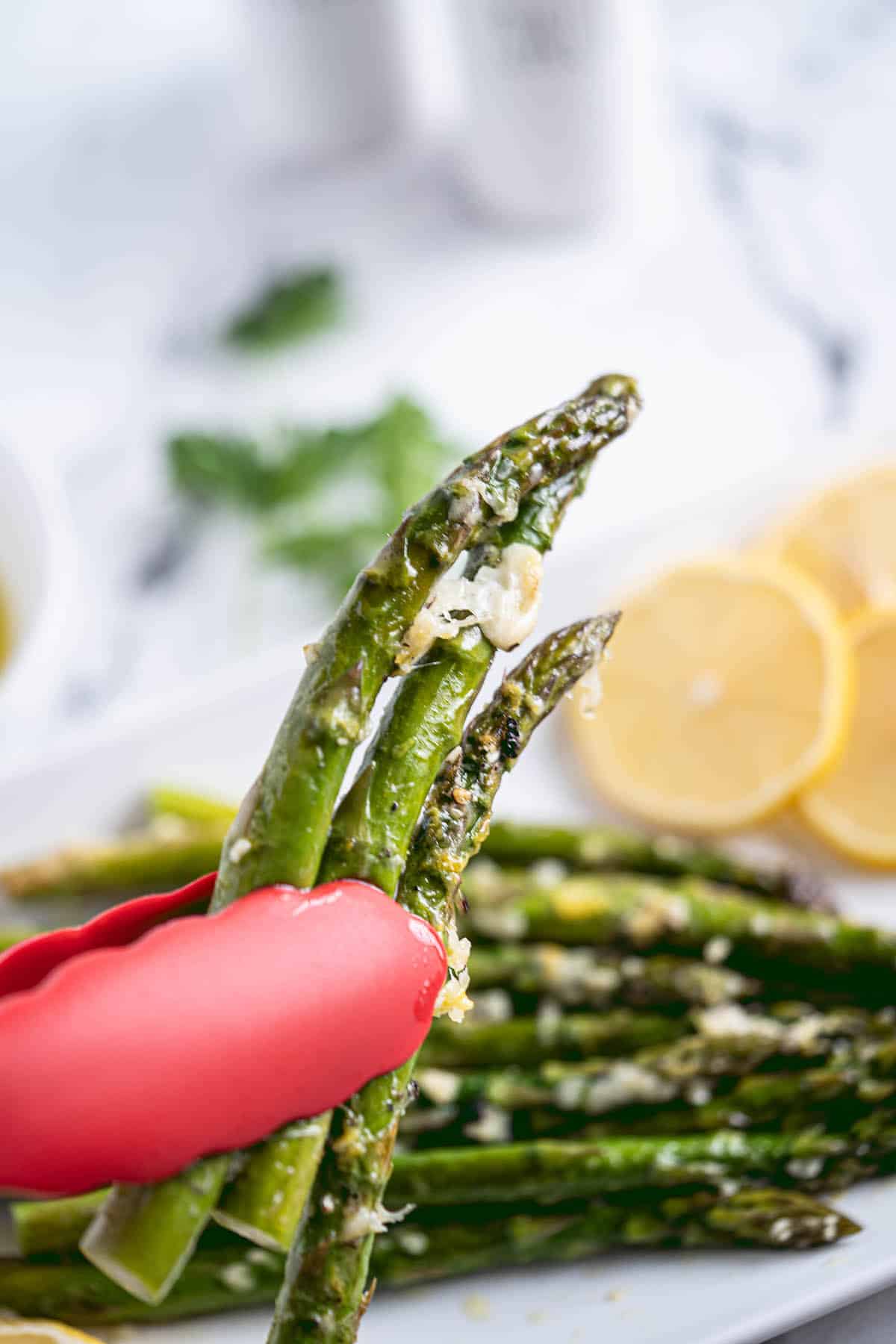 Tong holding spears of cooked asparagus.