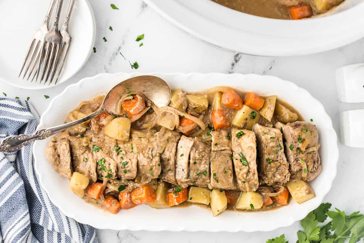 Sliced pork tenderloin with potatoes and carrots covered with gravy on a platter.