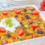 Cheesy Taco Hashbrown Casserole in a baking dish topped with olives, tomatoes, jalapenos, and sour cream.