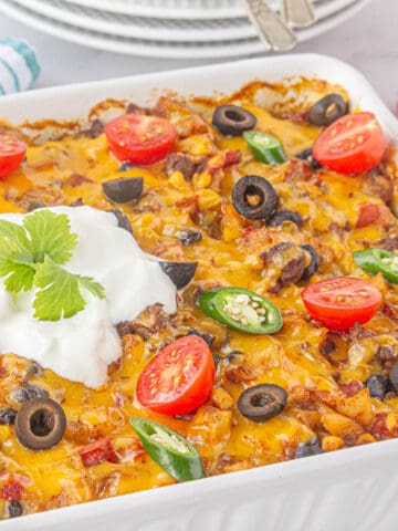 Cheesy Taco Hashbrown Casserole in a baking dish topped with olives, tomatoes, jalapenos, and sour cream.