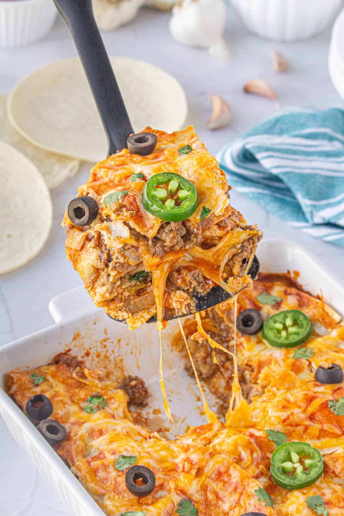 A spatula dishing up a serving of ground beef enchilada casserole.