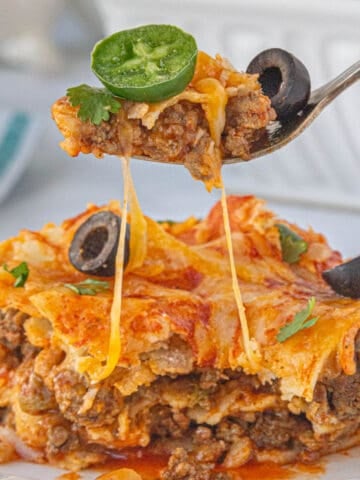 A serving of enchiladas on a plate with a fork taking a bite.
