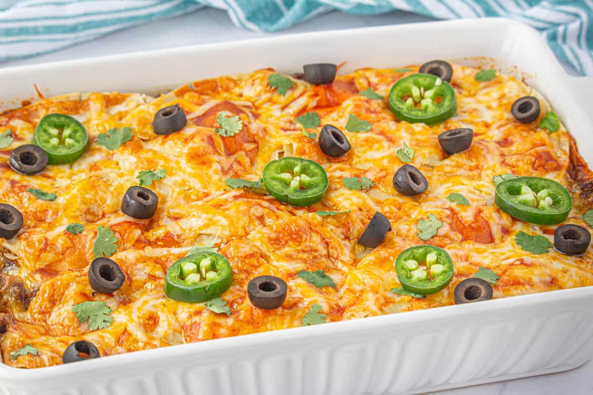 A casserole dish filled with enchiladas, topped with sliced olives and jalapenos.
