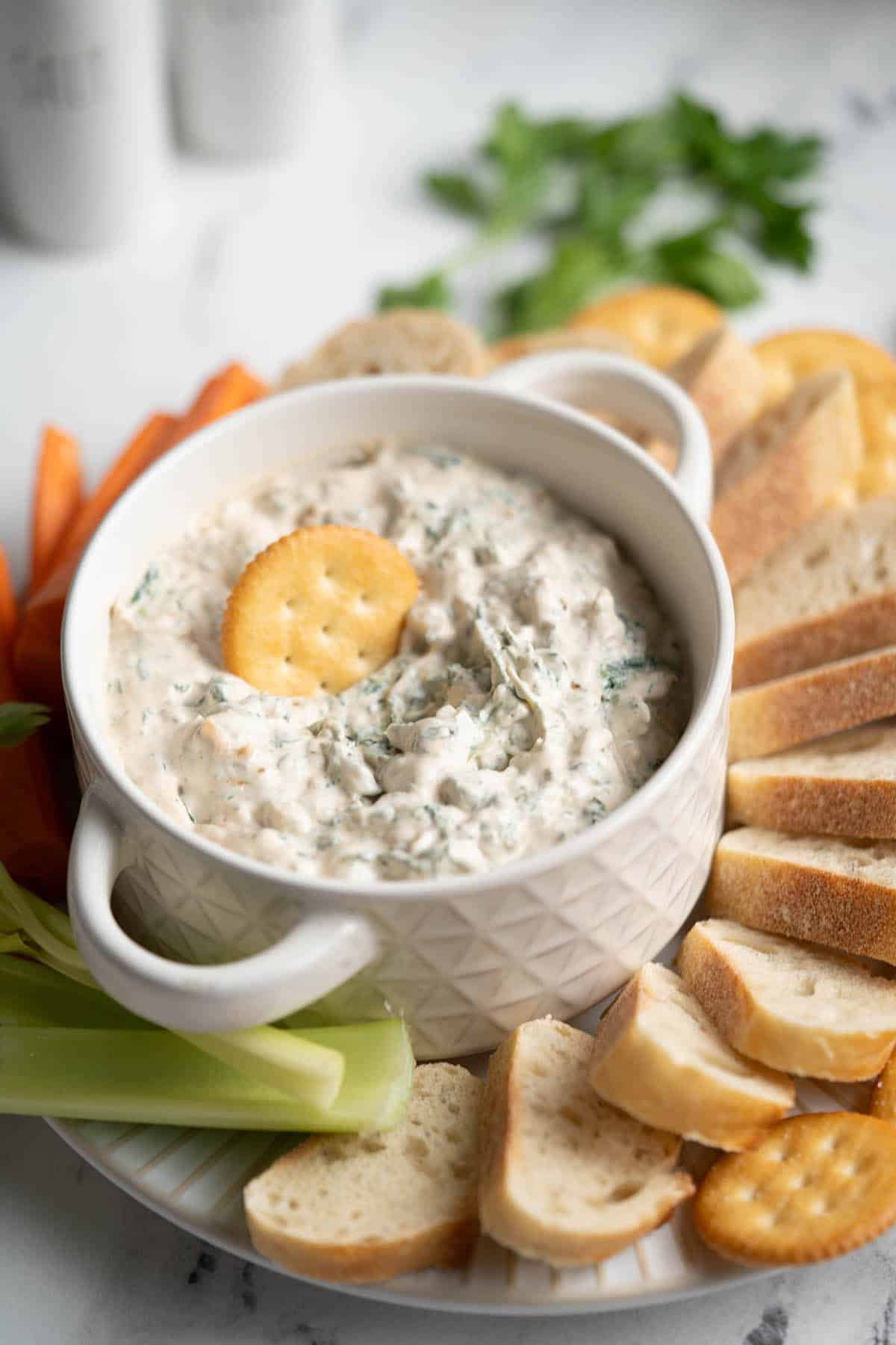 Spinach dip on a plate with bread and crackers for dipping.
