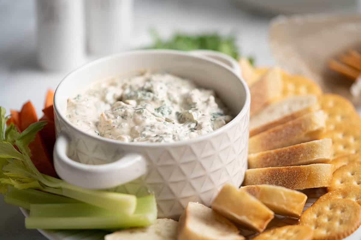 Spinach dip in a bowl surrounded by bread, cracker and vegetables for dipping.