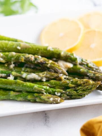 Slow Cooker Asparagus on a platter topped with melted cheese and garnished with lemon slices.