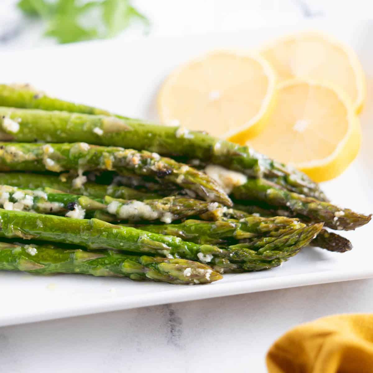 Slow Cooker Asparagus on a platter topped with melted cheese and garnished with lemon slices.