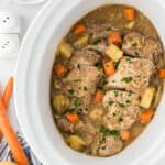 A crockpot filled with cooked, sliced pork tenderloin, potatoes and carrots with gravy.