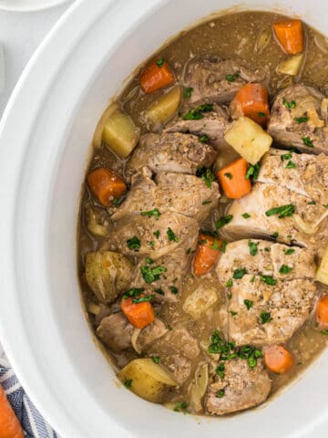 A crockpot filled with cooked, sliced pork tenderloin, potatoes and carrots with gravy.