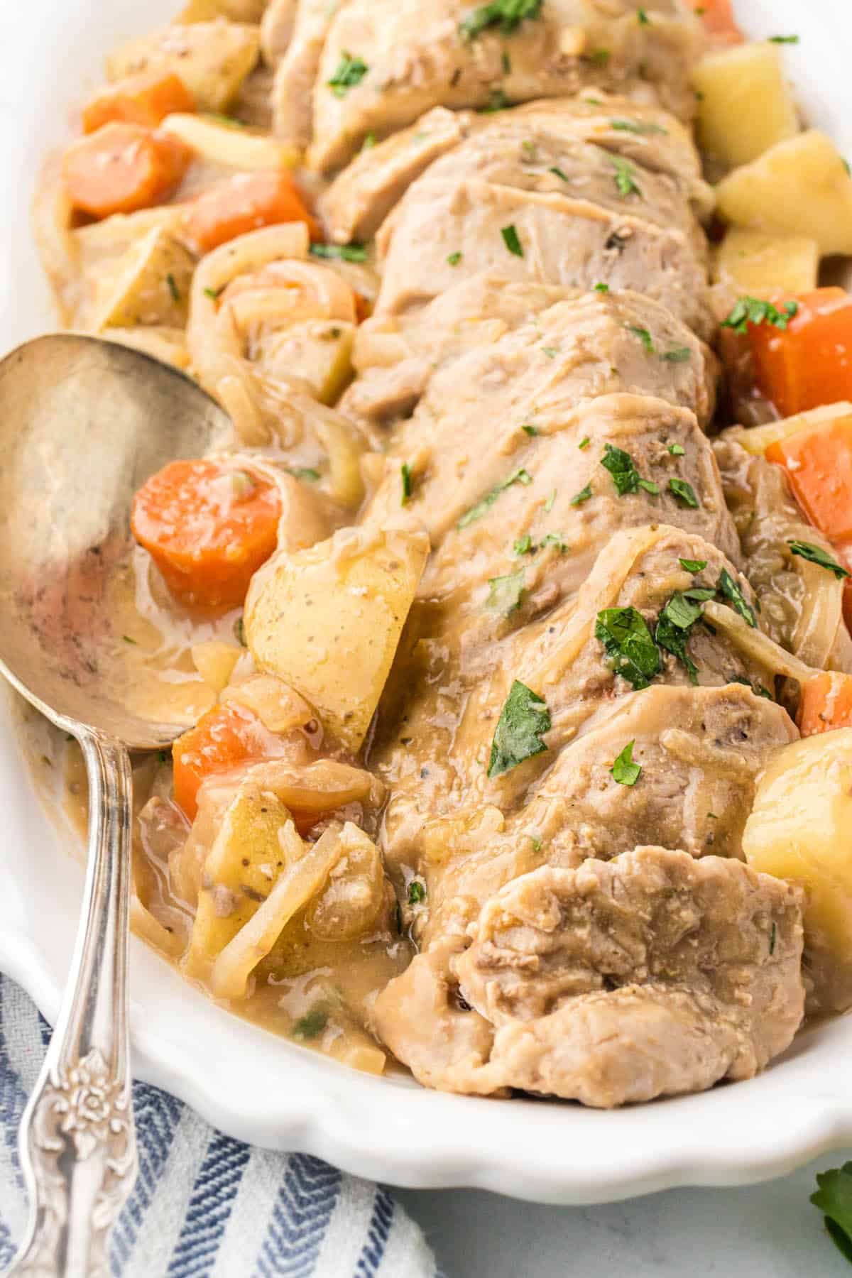 A white platter with sliced pork tenderloin, potatoes and carrots covered in gravy. A serving spoon is on the side.