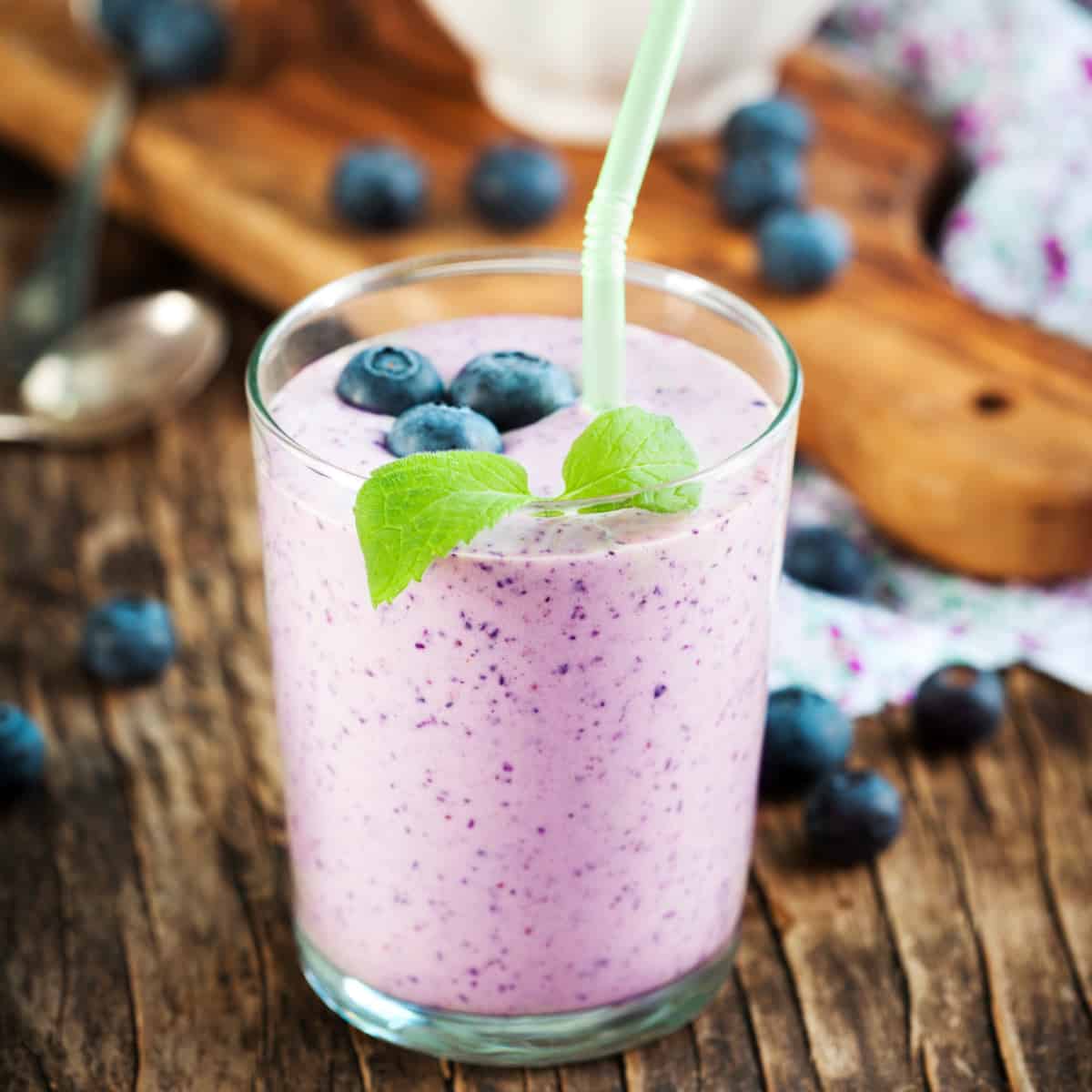 Blueberry Smoothie in a glass topped with whole blueberries. With a straw.
