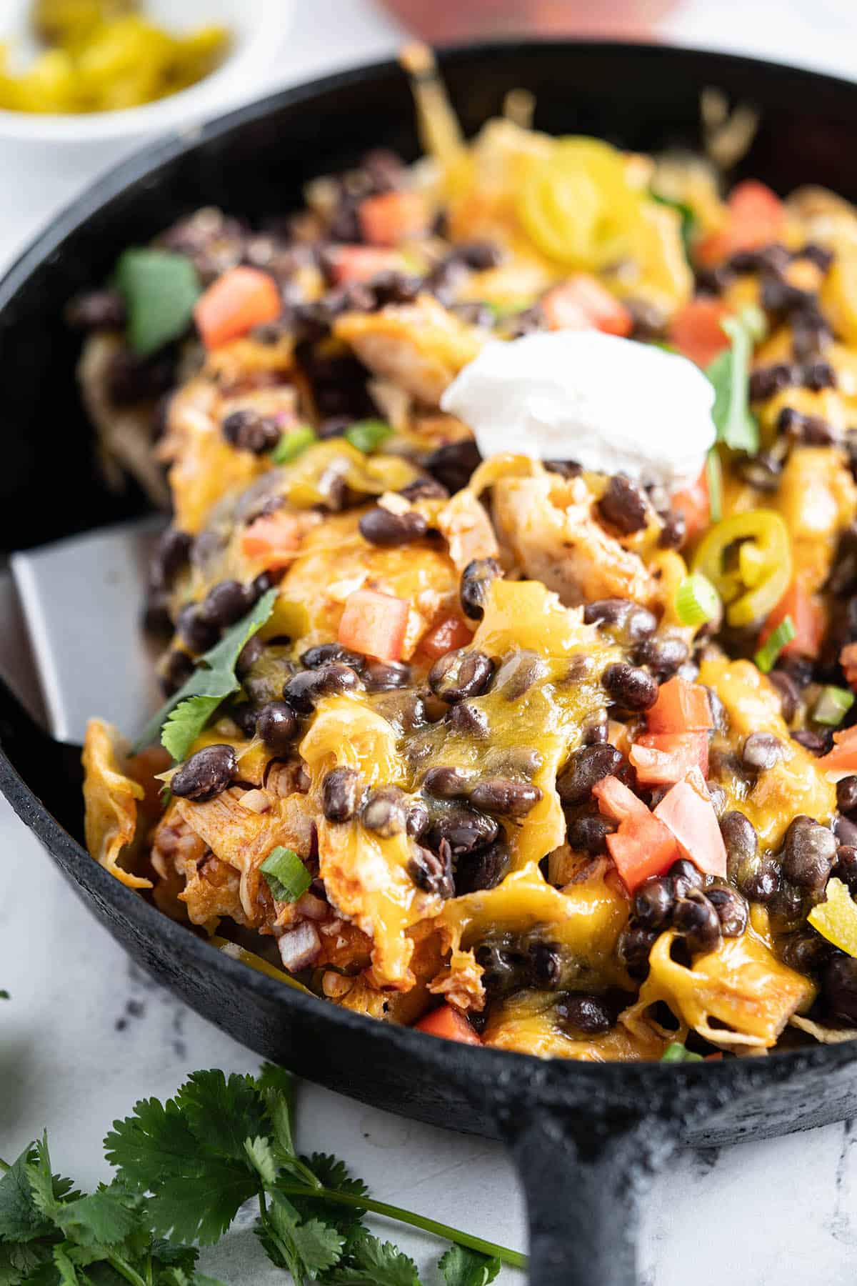 Cheesy Buffalo Wing Chicken Nachos in a skillet with a spatula for serving.