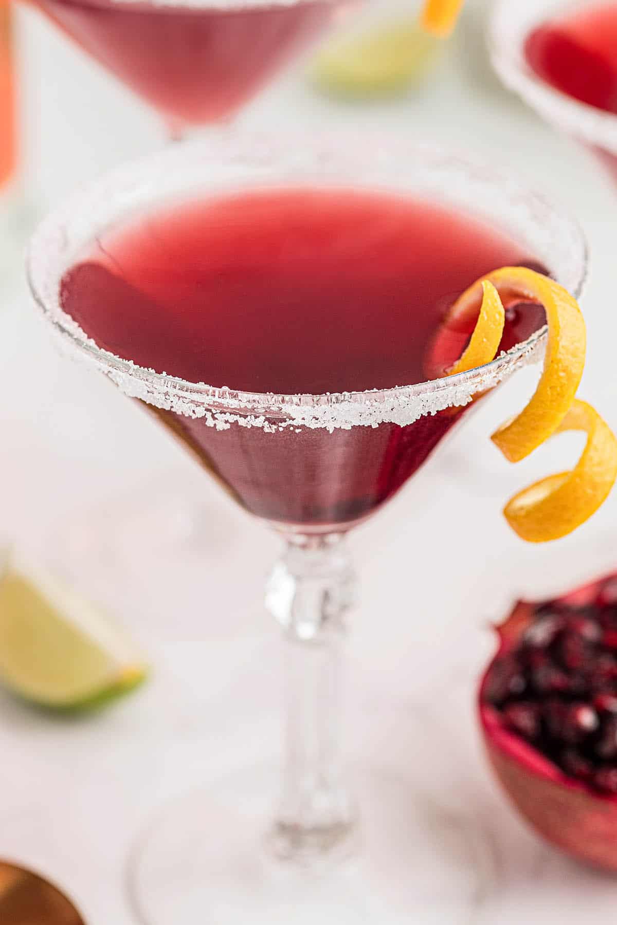 A pomegranate martini in a cocktail glass garnish with a twist of orange.