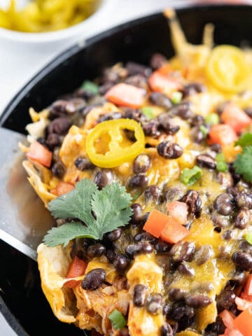 A pile of Buffalo Wild Wing Chicken Nachos in a skillet with a spatula dishing up a serving.