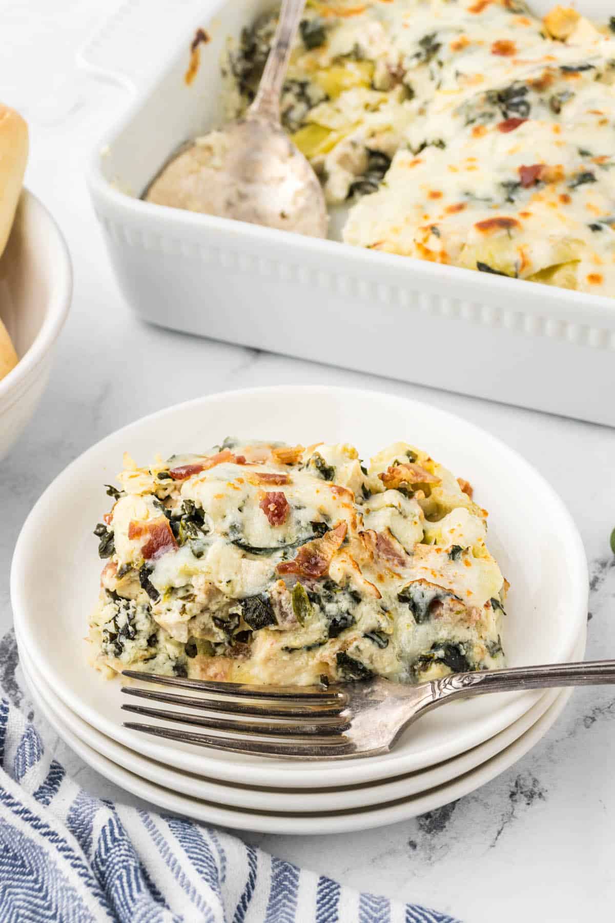 Plate with a serving of Chicken Spinach Artichoke Casserole dished up. With a fork on the side.