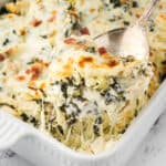 Creamy artichoke spinach chicken casserole in a baking dish with a serving spoon.