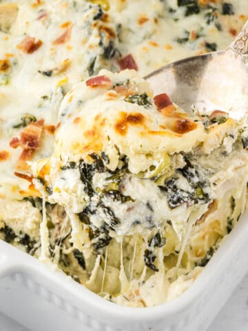 Creamy artichoke spinach chicken casserole in a baking dish with a serving spoon.