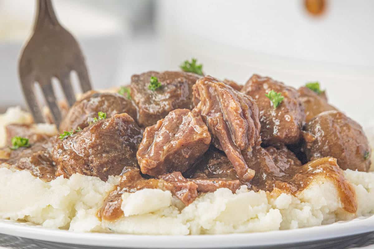 Steak bites and gravy over mashed potatoes with a fork on the side.