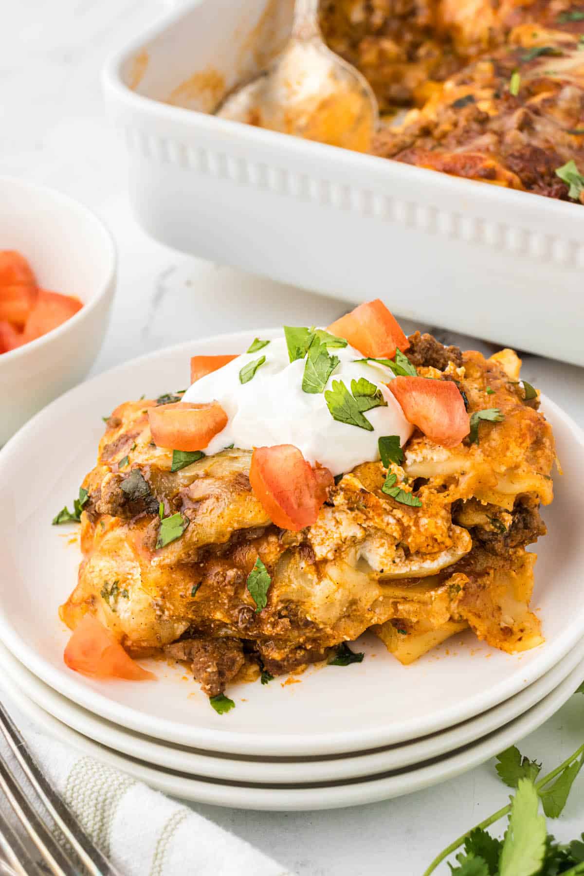 A serving of Taco Lasagna on a plate, with the rest of the casserole in the background.