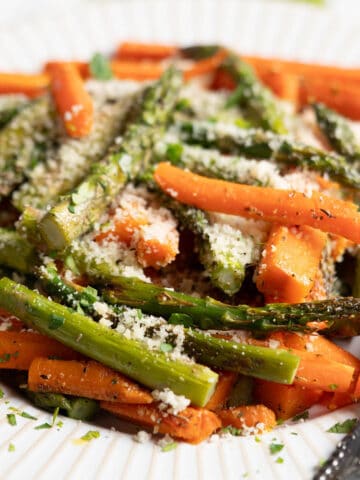 Roasted carrots and asparagus on a platter topped with grated parmesan cheese.