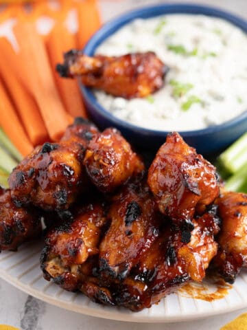 A platter filled with bbq chicken wings, carrots and celery. With dipping sauce.