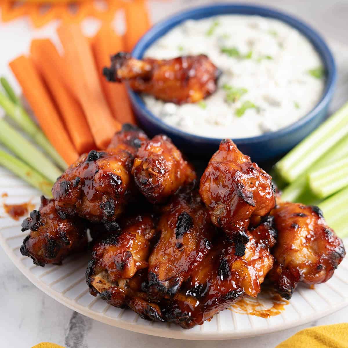 A platter filled with bbq chicken wings, carrots and celery. With dipping sauce.