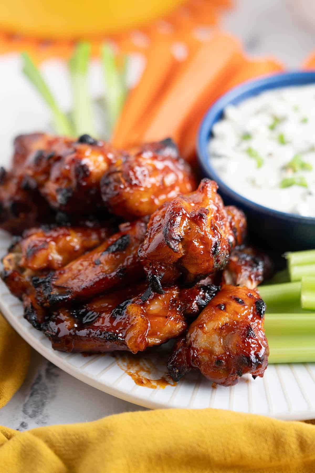 Chicken wings glazed in bbq sauce on a platter, served with carrots and celery. With a creamy dipping sauce.