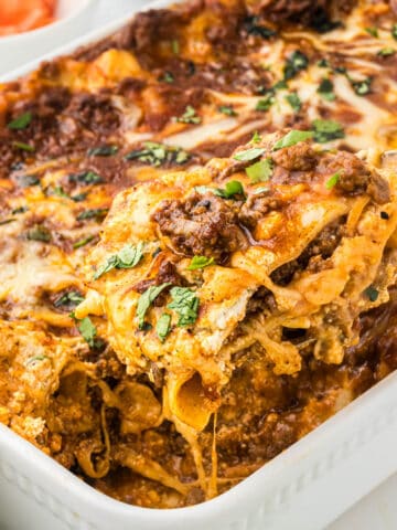 A casserole dish filled with Taco Lasagna, with a spatula dishing out a serving.