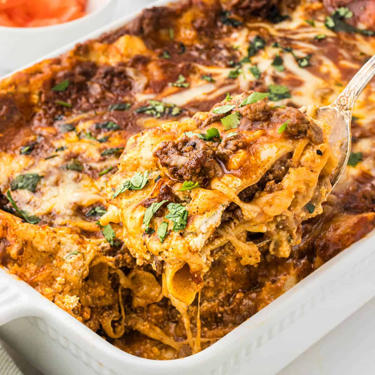 A casserole dish filled with Taco Lasagna, with a spatula dishing out a serving.