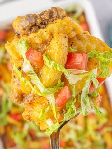 Close-up of a scoop of French Fry Casserole topped with tomatoes and lettuce.