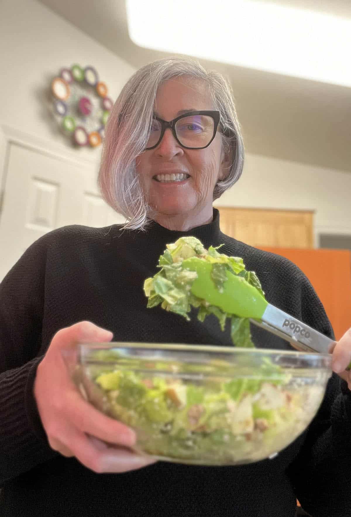 Blogger Deb Clark tossing the pear vinaigrette green salad in a large bowl with tongs.